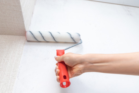 Primer of lijm wordt aangebracht met een brede roller op een muur.