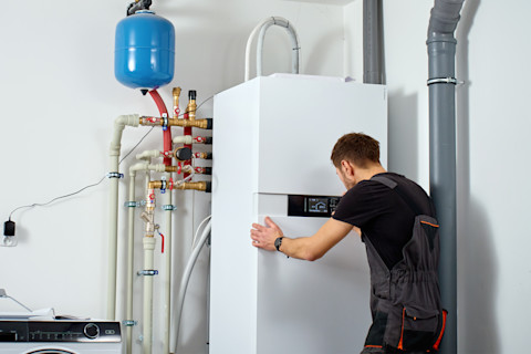 Monteur installeert een binnenunit van een warmtepomp en stelt het systeem af. Leidingen en een expansievat zijn zichtbaar als onderdeel van de installatie.