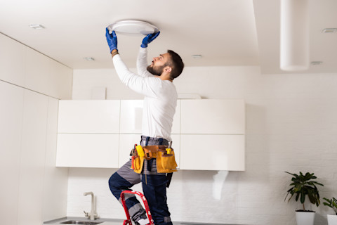 Een elektricien monteert een witte lamp na reparatie tegen het plafond