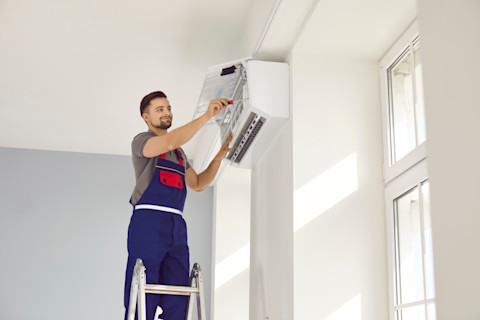 Monteur installeert een airconditioningsysteem aan een muur in een woning, zichtbaar met gereedschap en uniform.