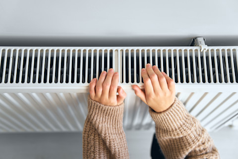 Kind in een wollen jas warmt handen aan een radiator.
