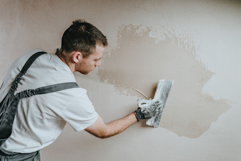 Bouwvakker in overall brengt stucwerk aan op een binnenmuur.