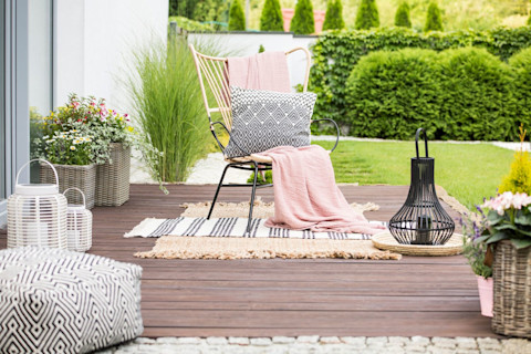 Witte kussens en een roze plaid op een houten vlonder, sfeervol ingericht als loungeplek.