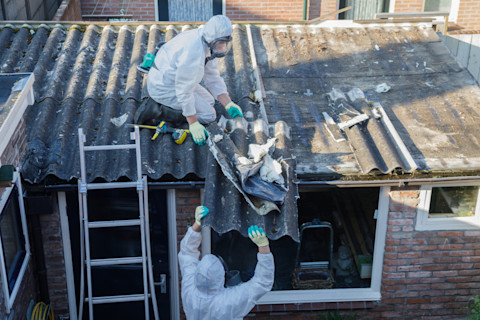 Werknemer in beschermende kleding verwijdert asbestplaten van een dak
