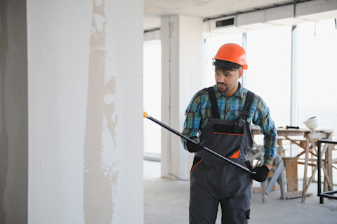 Een stukadoor in een oranje helm en blauw-oranje overall bewerkt een muur.