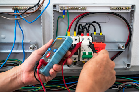 Een elektricien controleert met een multimeter het spanningsniveau in een woning voor nauwkeurige meting.