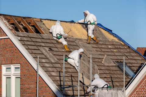 Werknemer in beschermende kleding verwijdert asbestplaten van een dak