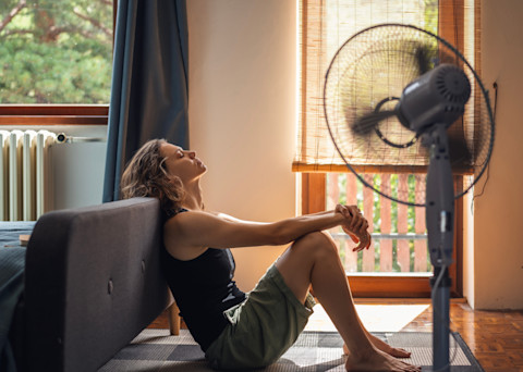 Jonge vrouw lijdt zichtbaar onder de hitte terwijl ze zwetend op de bank in haar warme huis zit.