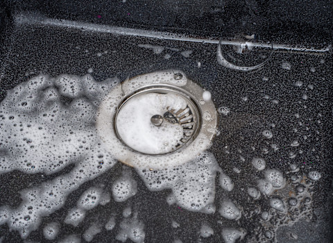 Schuimend water stroomt in een afvoerputje, duidelijk teken van ophoping of verstopping.