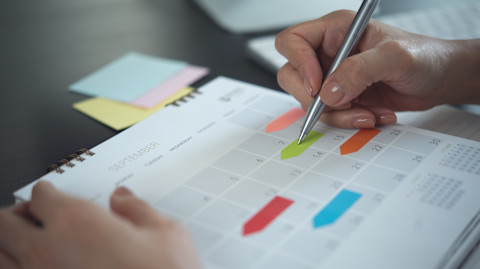 Hand van een vrouw die een tuinkalender voor 2026 invult met een pen in een notitieboek.