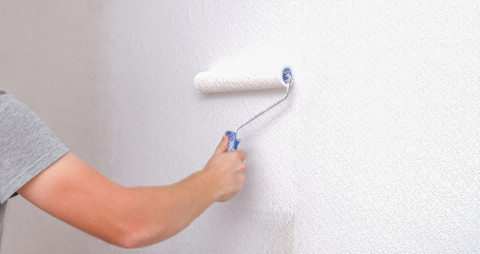 Man brengt renovliesbehang aan op een witte muur met lijmroller