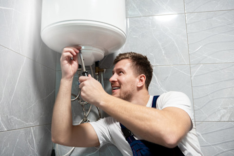 Jonge man in werkoverall glimlacht vriendelijk, klaar om onderhoud of reparatiewerkzaamheden uit te voeren.