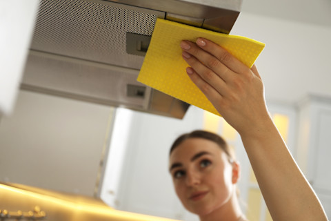 Jonge vrouw maakt de buitenkant van een afzuigkap schoon in een moderne keuken.