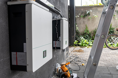 Installatie van een thuisbatterij met omvormer naast een wand met zonnepanelen in een woning.