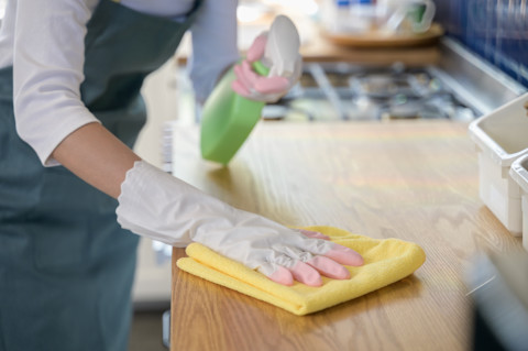 Vrouw met rubberen handschoenen maakt een houten keukenblad schoon met een doekje.