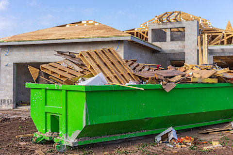 Een container met puin die voor een huis staat om een dakbeschot te gaan vervangen