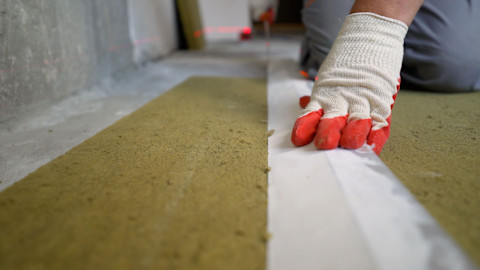 Werknemer plaatst isolatiemateriaal tussen houten vloerbalken in kruipruimte