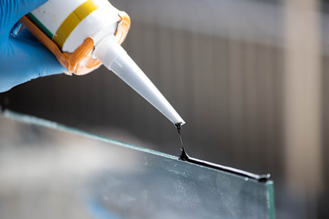 Close-up van een siliconenkitpistool waarbij de kit strak wordt aangebracht op glas.