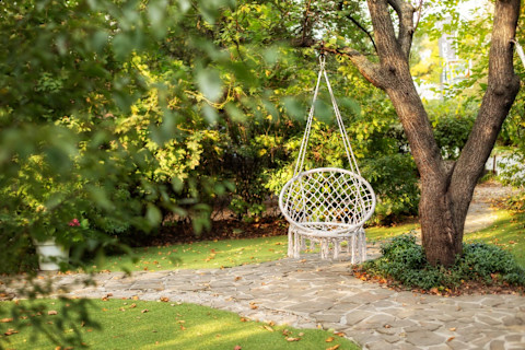 Hangende rotan stoel in een bohemian tuin op een zonnig terras, ideaal om te ontspannen.