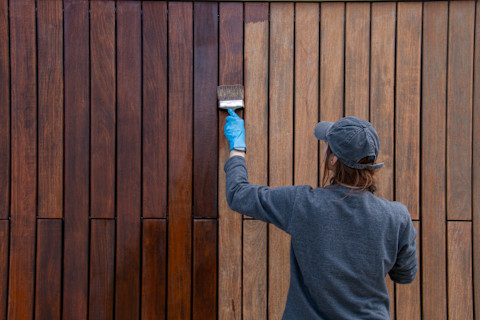 vrouw beitst een hoge bruine houten schutting