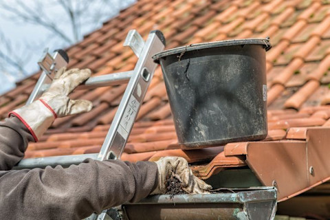 Vakman op ladder maakt de dakgoot schoon en verwijderd bladeren