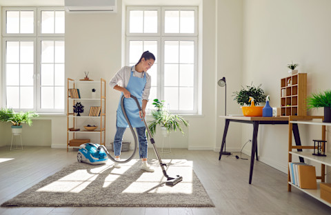 Vrouw met stofzuiger en handschoenen maakt de woonkamer schoon in een netjes opgeruimd huis.
