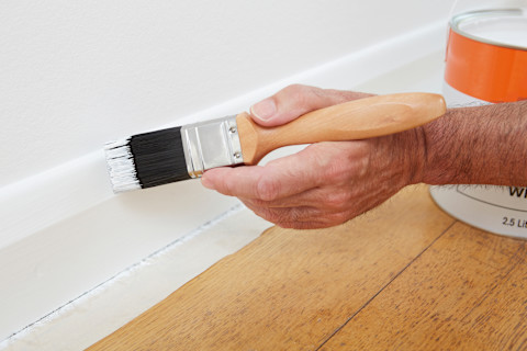 Man schildert de plinten van een houten vloer wit.