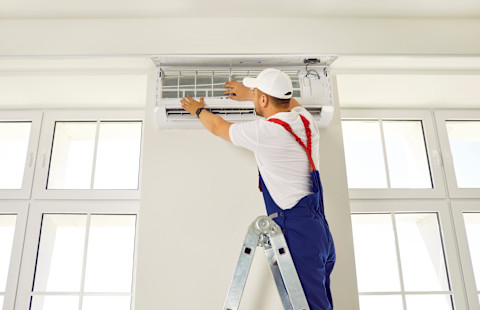 Een vakman voert airco onderhoud uit in een blauwe overal.