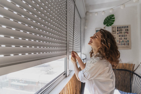 Vrouw sluit rolluiken aan de buitenkant van een woning, zicht op moderne gevel en rolluikmechanisme.