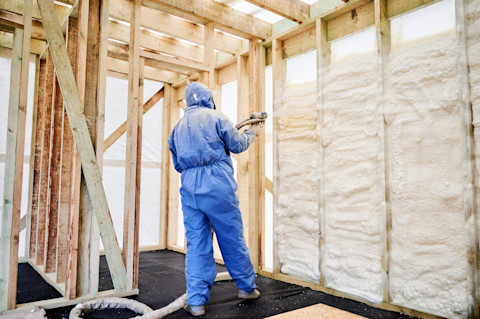 Een medewerker spuit purschuim aan in een wand voor isolatie. Hij draagt beschermende kleding.
