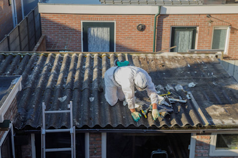 Een specialist verwijdert asbest van een dak terwijl hij beschermende kleding draagt.
