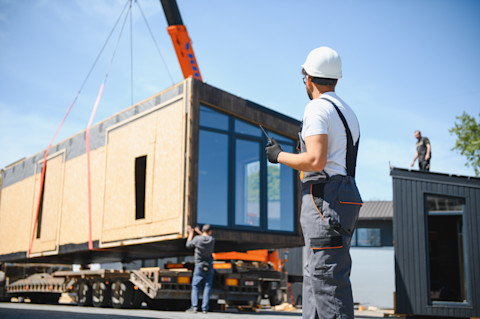 Bouwvakker houdt toezicht op de plaatsing van een prefab dakkapel op het dak van een woning.