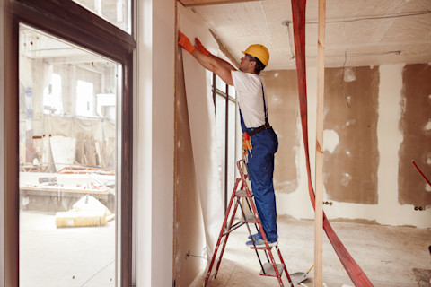 Behanger brengt renovliesbehang aan op een muur in een nieuwbouwwoning, gefocust op nauwkeurige afwerking.