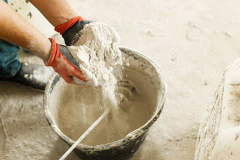 Werker mengt gipspleister met water in een emmer voor stucwerk.