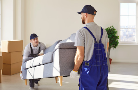 Twee professionele verhuizers tillen een bankstel een woning binnen, symbool voor een volledige verhuisservice aan huis.