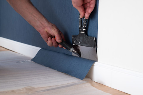 Man snijdt behang op maat tijdens renovatiewerk, met focus op precisie en voorbereiding van de muur.