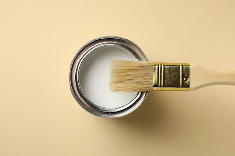 Verfblik en kwast op een beige achtergrond, klaar voor schilderwerk