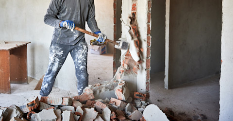 Close-up van een sloophamer die een bakstenen muur met pleisterwerk inslaat, zichtbaar moment van sloopwerk.