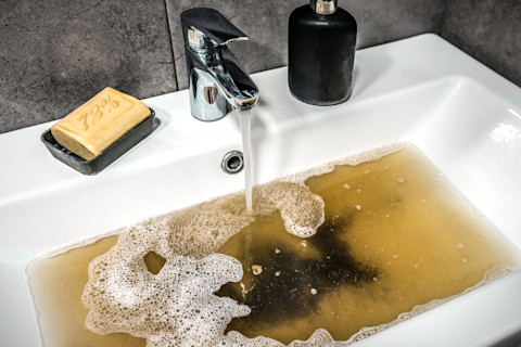 Vuil water in een wastafel geeft een typische bruine brij van zeepresten en verstopping weer.