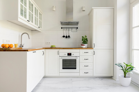 Een minimalistische witte keuken met zilveren afzuigkap en plant op de grond.
