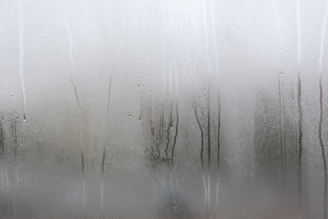 Condensdruppels op een raam na een hevige regenbui, met wazig uitzicht naar buiten en beslagen glas.