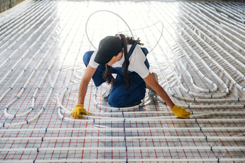 Monteur legt kunststof leidingen voor een vloerverwarmingssysteem op de ondervloer.