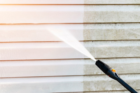 Gevelreiniging met een hogedrukreiniger, een schoonmaker spuit water tegen de gevel om vuil en aanslag te verwijderen.
