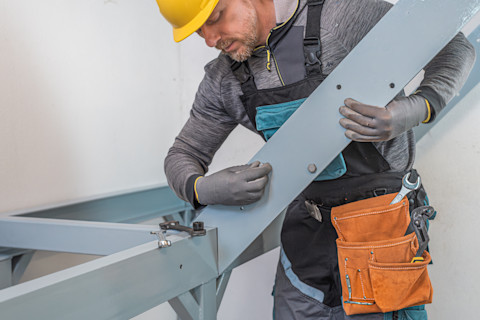 Een vakman monteert een trap, hij plaatst een onderdeel van de trapconstructie.